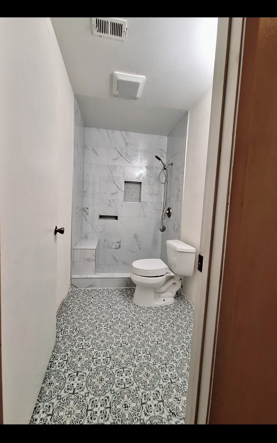 Bathroom with marble-look tiled shower, patterned floor tile and toilet