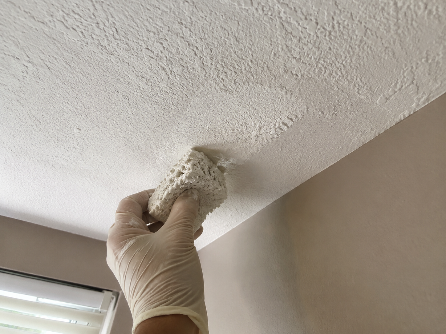 Worker scraping a popcorn ceiling in an empty room